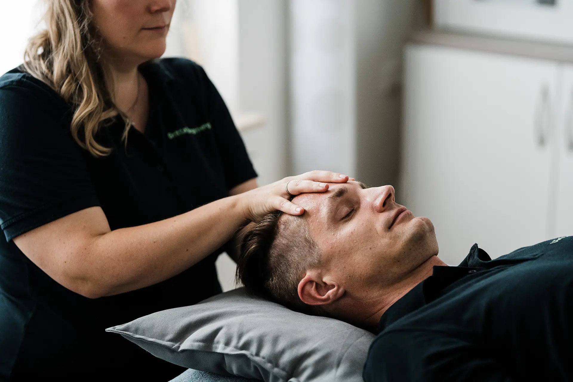 Physioteam Dewald Hungerberg Detailfoto einer Behandlung, die Therapeutin hat die Hände auf der Stirn des Patienten